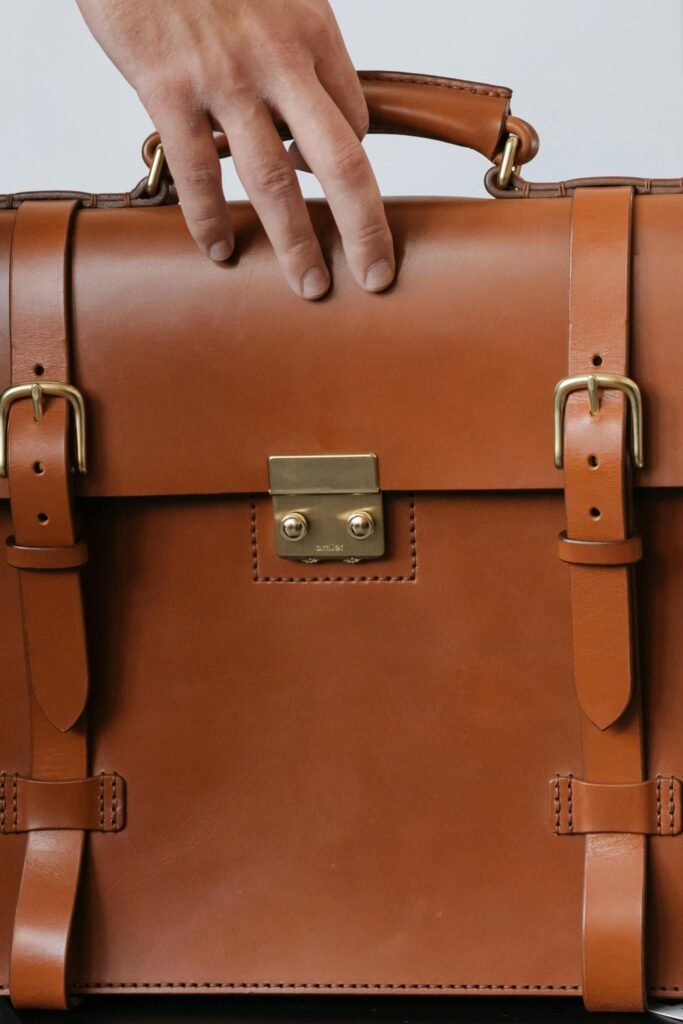 Close-up of a hand holding a stylish brown leather briefcase indoors.